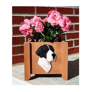 May include: A wooden planter box with a black and white English Pointer dog head sculpture on the front. The planter is filled with pink flowers.