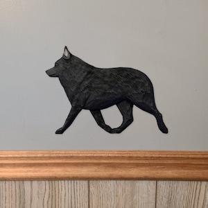 Puede incluir: Una talla de madera negra de un Shetland Sheepdog caminando hacia la derecha. La talla está montada en una pared con un marco de madera.