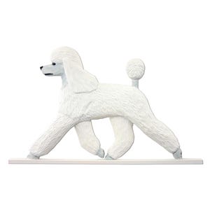 May include: A white poodle figurine standing on a flat rectangular base. The dog is depicted in a side profile view with a textured coat, a pom-pom tail, and a black nose. The sculpture is crafted with detailed fur carvings and stands on a white base.
