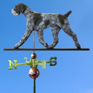 May include: A brown and white German Shorthaired Pointer dog weathervane with a copper colored arrow and a copper colored ball on top of the arrow. The weathervane is mounted on a wooden post.