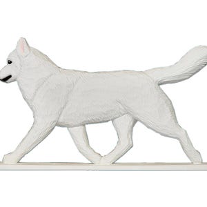 Pu&ograve; includere: Figurina di legno bianco di un cane husky che cammina. La figurina &egrave; su una base bianca.