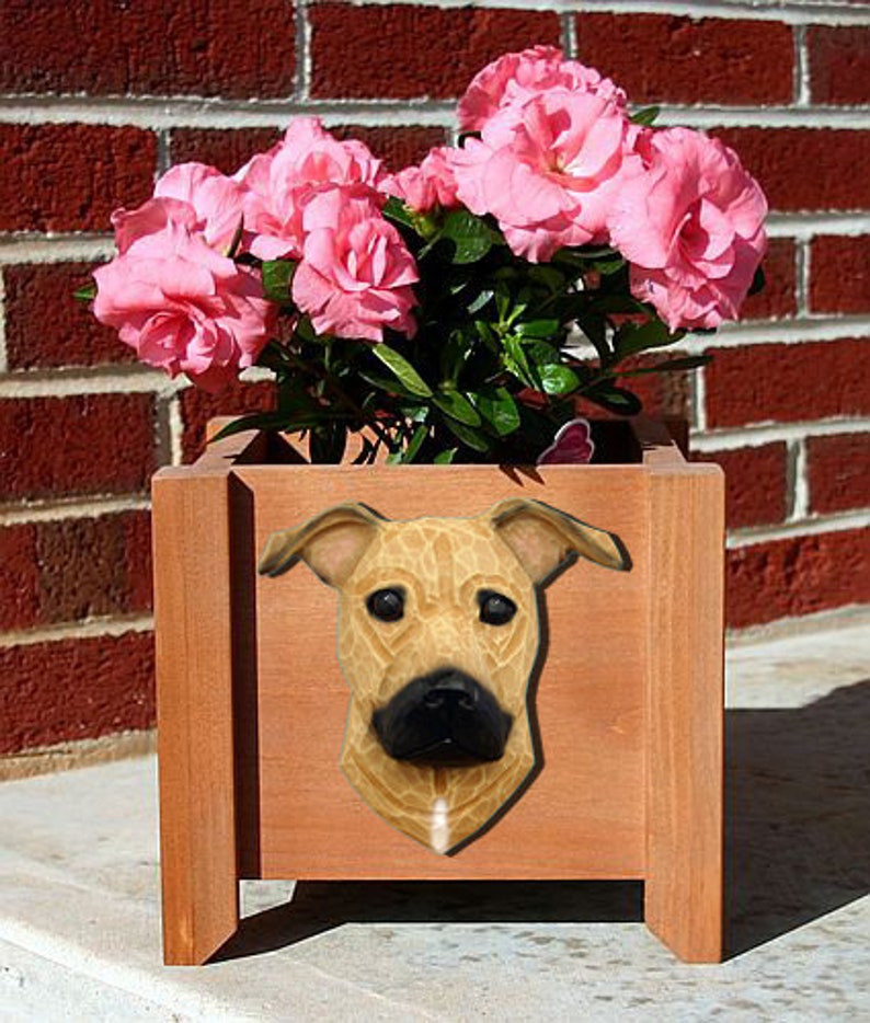 May include: A wooden planter box with a brown dog's head sculpture on the front. The planter is filled with pink flowers.