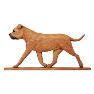 May include: A carved wooden figurine of a dog in a walking pose, featuring a light brown finish with visible chisel marks and a dark brown muzzle. The dog is mounted on a thin, rectangular wooden base, capturing a side profile view.