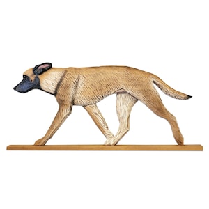 Puede incluir: Escultura de madera de un perro en posición de caminar. El perro es de color marrón claro con detalles negros en las orejas y el hocico. Está montado sobre una base rectangular de madera, sobre un fondo blanco.