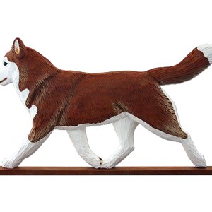 Pu&ograve; includere: Una statuetta di legno di un cane Husky siberiano marrone e bianco che cammina su una base di legno. Il cane &egrave; dipinto con dettagli realistici, tra cui il suo pelo e i suoi occhi.