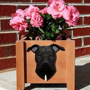 May include: A black dog planter with a brown wooden planter box. The planter box is filled with pink flowers.