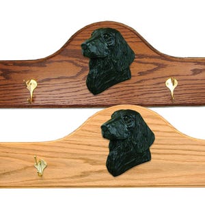 May include: A wooden coat rack with three hooks features a black flat-coated retriever dog head sculpture. The rack is available in two wood finishes: dark brown and light brown.