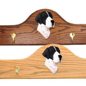 May include: A wooden coat rack with three hooks features a black and white English Pointer dog head sculpture. The rack is made of oak wood and has a natural finish.