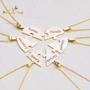 Puede incluir: Collares dorados con colgantes de piezas de rompecabezas, cada uno grabado con un nombre. Los colgantes están conectados a delicadas cadenas doradas. Los nombres incluyen "Karma", "Natalie", "Layzonic", "Kariele" y "Danyele".