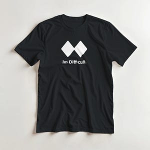 May include: Black t-shirt featuring a white graphic of two connected diamond shapes and the text "Im Difficult." The shirt has a crew neck and short sleeves. The design is centrally placed on the front of the garment.