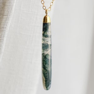 May include: A gold chain necklace with a long, teardrop-shaped green and white agate pendant.