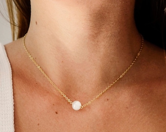May include: A delicate gold chain necklace with a single white pearl pendant.