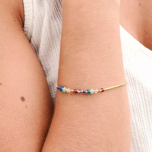 May include: A gold chain bracelet with small, colorful beads. The bracelet is on a person's wrist.