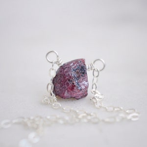 May include: A silver chain necklace with a raw, pink ruby gemstone pendant.