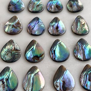 Puede incluir: Una colecci&oacute;n de 16 colgantes en forma de l&aacute;grima de concha de abul&oacute;n iridiscente. Las conchas son una mezcla de colores azules, verdes y morados con un acabado nacarado.