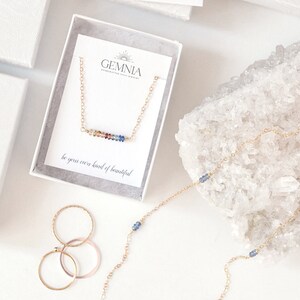 Puede incluir: Un collar de oro con una barra de piedras preciosas de colores y el texto "be your own kind of beautiful". El collar est&aacute; en una caja blanca con el texto "GEMNIA handcrafted jewelry".