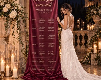 May include: A tall, deep red fabric wedding seating chart banner featuring the gold text Please find your table, Amelia & James, June 19, 2027, and a list of guest names organised by table numbers, displayed on a stand.