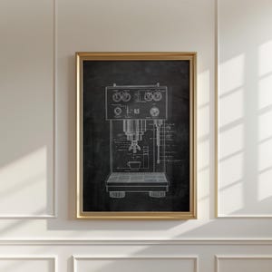 May include: A framed print of an espresso machine diagram in white on a black background. The diagram shows the internal components and design of the machine. The frame is gold-colored, and the print is displayed on a white wall.