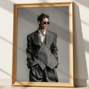 May include: A framed portrait of a person wearing a gray suit with a unique, layered design. The suit includes a blazer, vest, and trousers. The person is wearing sunglasses and a white collared shirt. The frame is made of light-colored wood.
