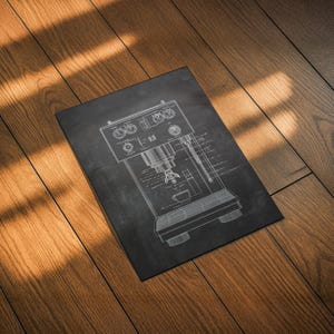 May include: A black rectangular print featuring a detailed white line drawing of an espresso machine. The machine's components, including dials, a portafilter, and a cup, are clearly depicted. The print is set against a dark background.