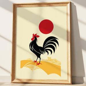 Op de afbeelding: Ingelijste kunstprint met een gestileerde zwarte haan met een rode kam en poten, tegen een gele achtergrond en een rode zon. Het kunstwerk is in minimalistische stijl en is ingelijst in licht hout.