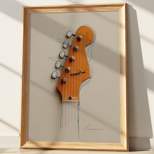 May include: Framed art print featuring a stylized illustration of a guitar headstock. The artwork showcases the headstock in a warm orange hue, with black line art outlining the shape and details. The print is encased in a light brown wooden frame.
