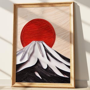 May include: Framed artwork featuring a red sun and a mountain, likely Mount Fuji, rendered in a paper quilling style. The mountain is depicted in black, white, and gray, with a light beige background. The artwork is encased in a light brown wooden frame.