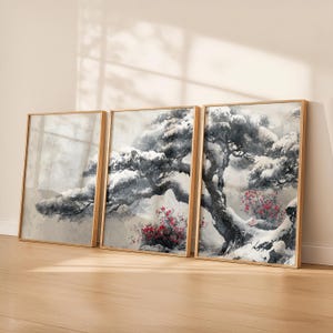 May include: Three framed art prints showcasing a winter scene with snow-laden trees and red flowers. The artwork is set against a muted background. The frames are a light wood colour, creating a tranquil and natural aesthetic.