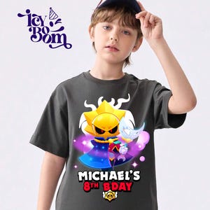 May include: Dark gray t-shirt featuring a cartoon sun character with a cape and a weapon, with the text "MICHAEL'S 8TH BDAY". The shirt also has the text "Icy Bom" in the upper left corner. The shirt is worn by a person.