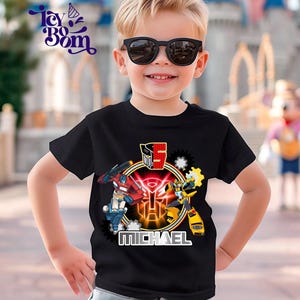 May include: A black t-shirt featuring a colorful graphic of Transformers characters, including Optimus Prime and Bumblebee, with the number 5 and the name "MICHAEL". The shirt is worn by a young child wearing sunglasses.