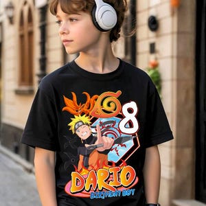 May include: Black t-shirt featuring a colorful graphic of an anime character with the number 8 and the name "Dario, Birthday Boy". The design includes orange, yellow, and blue accents. The shirt is worn by a person wearing white headphones.