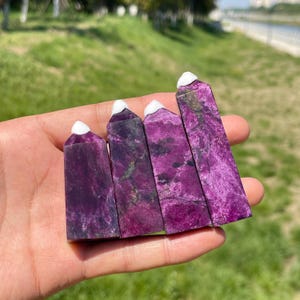 May include: Four polished crystal towers featuring a deep magenta and purple hue with dark mineral inclusions and a distinct white cap at the pointed tip. These four vertical stone specimens are arranged side by side in a row.