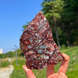 May include: A triangular-shaped mineral specimen featuring a translucent pale green base with a dense network of deep red, web-like inclusions throughout the surface. The stone has a jagged, uneven edge and a crystalline, fractured texture.