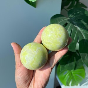 May include: Two smooth, spherical stones with a polished finish. The stones feature a vibrant chartreuse and pale yellow marbled pattern with subtle white veining throughout, creating a bright, consistent appearance across both rounded surfaces.