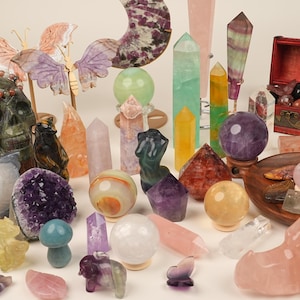 Peut inclure: Une collection de cristaux et de pierres précieuses de formes et de couleurs variées. Comprend des sphères, des pyramides, des obélisques et des figurines sculptées, comme un crâne et des papillons. Les cristaux sont dans des tons de violet, vert, jaune et rose. Mesures en centimètres.
