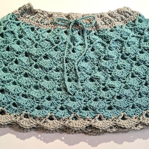 May include: A teal and grey crochet skirt with a scalloped hem and drawstring waist. The handmade skirt has a textured, open crochet pattern. The skirt is a unique, handcrafted item.