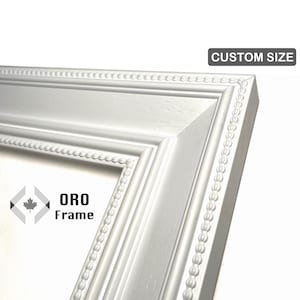 May include: Close-up of a white picture frame corner with a beaded edge. The frame has a detailed design and the text "CUSTOM SIZE" is in the upper right corner. The logo "ORO Frame" is in the lower left corner.