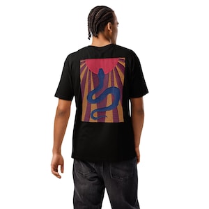 May include: Black t-shirt featuring a vibrant graphic on the back. The design showcases a blue snake against a backdrop of a red sunburst with orange and purple rays. The shirt is a classic crew neck style.