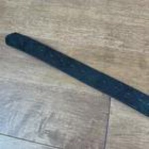 Op de afbeelding: Een zwarte golfclubgrip met een getextureerd oppervlak. De grip is cilindrisch en ontworpen om een veilige grip te bieden. De grip ligt op een lichtbruin houten oppervlak.