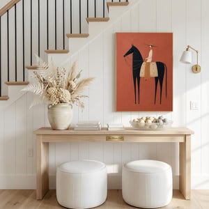 Folk art print of a figure in a wide-brim hat riding a tall dark horse with a tan saddle blanket on a warm terracotta background, vertical mid century equestrian wall art.