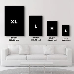 以下が含まれることがあります： XL (60x90 cm), L (50x75 cm), M (40x60 cm), S (30x45 cm) のラベルが付いた 4 つの黒い長方形のキャンバス。白いソファと灰色のラグの上にキャンバスが表示されています。