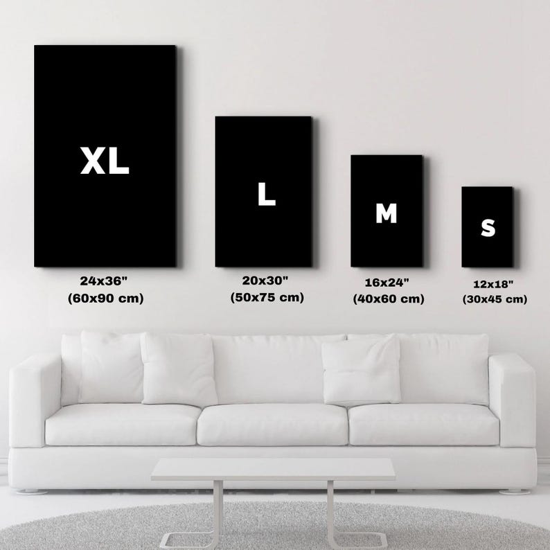 以下が含まれることがあります： XL (60x90 cm), L (50x75 cm), M (40x60 cm), S (30x45 cm) のラベルが付いた 4 つの黒い長方形のキャンバス。白いソファと灰色のラグの上にキャンバスが表示されています。