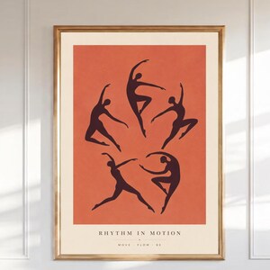 Puede incluir: Una lámina enmarcada con cinco siluetas negras de bailarines en varias poses sobre un fondo naranja terracota. El texto RHYTHM IN MOTION y MOVE FLOW BE está impreso en negro en la parte inferior del borde de color crema.