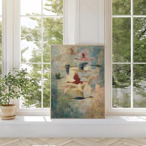 May include: A framed art print featuring a flock of birds in flight. The artwork showcases birds with various colors, including red, pink, and blue, against a muted blue and green background. The print is displayed on a white windowsill near a window with a view of trees.