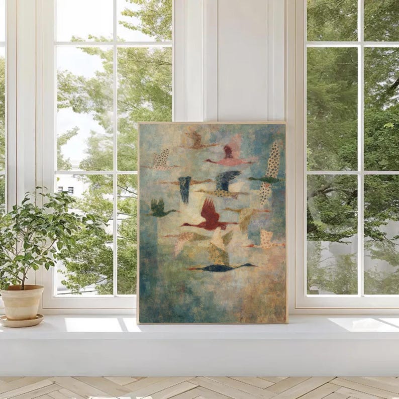 May include: A framed art print featuring a flock of birds in flight. The artwork showcases birds with various colors, including red, pink, and blue, against a muted blue and green background. The print is displayed on a white windowsill near a window with a view of trees.