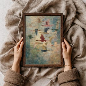 May include: A framed art print featuring a flock of birds in flight. The birds are depicted in various colors, including red, blue, and green, against a textured, blue-green background. The artwork is held by a person.