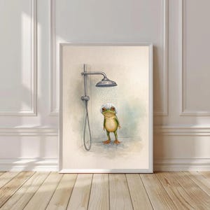 Peut inclure: Impression artistique encadrée représentant une grenouille sous la douche. La grenouille verte, coiffée d'un bonnet de douche blanc, se tient sous un pommeau de douche argenté. L'œuvre est posée sur un fond neutre, créant une scène humoristique.