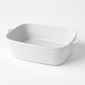 May include: A white rectangular baking dish with rounded corners and small handles. The dish has a ribbed exterior and a smooth interior. This ceramic bakeware is suitable for casseroles and other baked dishes.
