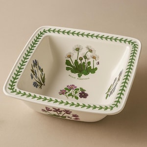 May include: Square ceramic serving dish with a white background and a green leaf border. The dish features botanical illustrations of flowers in shades of purple, white, and green. The text "BULIS PERENNIS" is also visible.