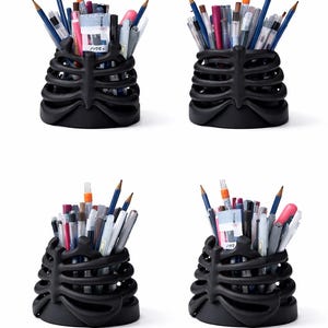 May include: Four black desk organizers shaped like a human rib cage, each filled with various pens, pencils, and markers. The matte black containers feature curved, horizontal rib-like structures that hold writing instruments upright.